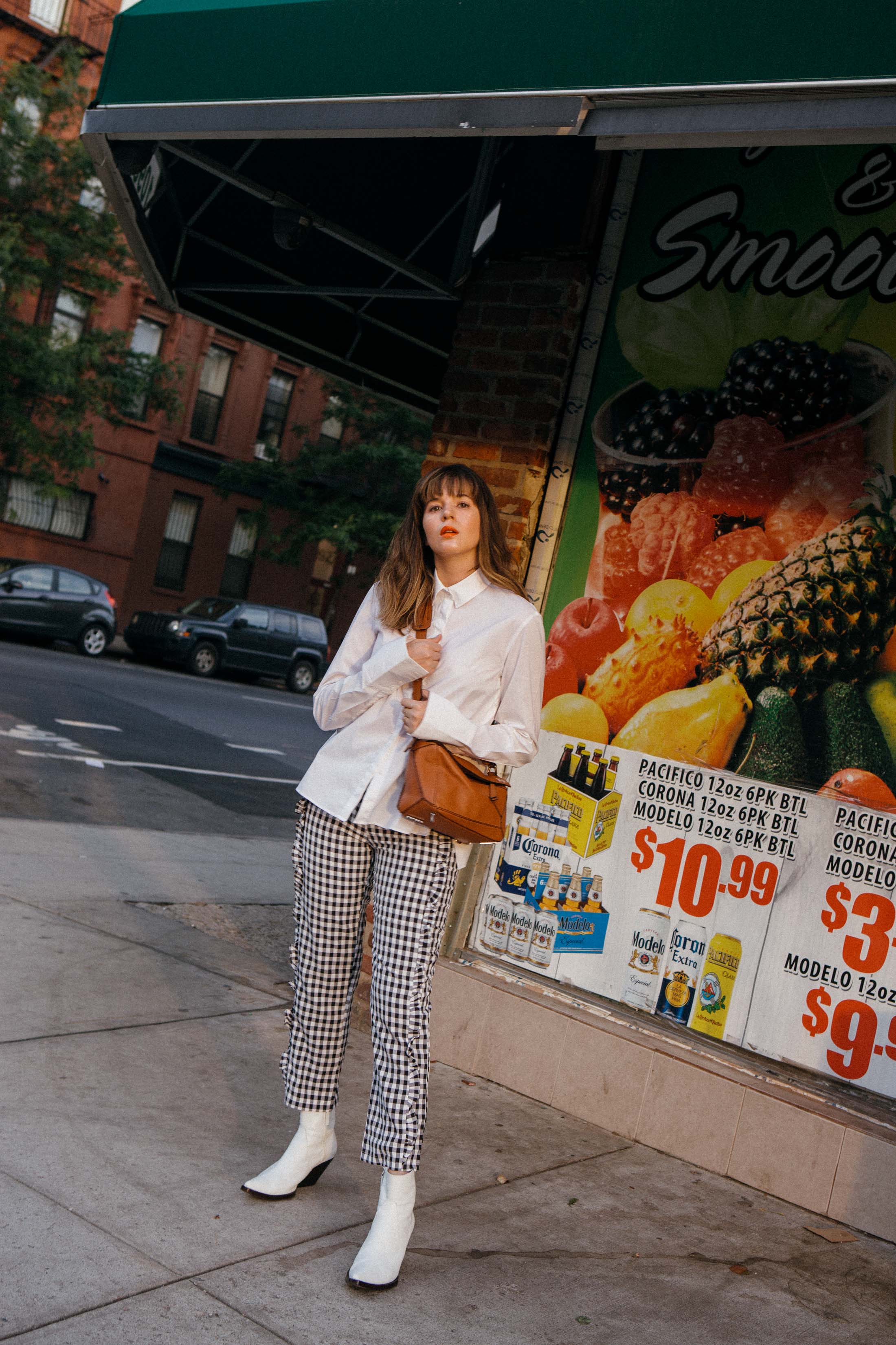 Maristella wears a shirt from H&M, gingham pants from Alpha and Omega, white cowboy boots from Zara and a tan leather Loewe Puzzle Bag