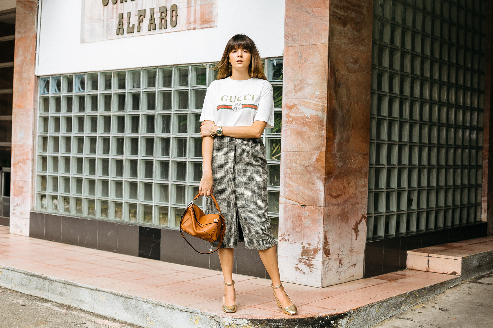 Maristella wears a Gucci logo tee, plaid wool button front skirt from MaxMara, Loewe bag and gold block heels