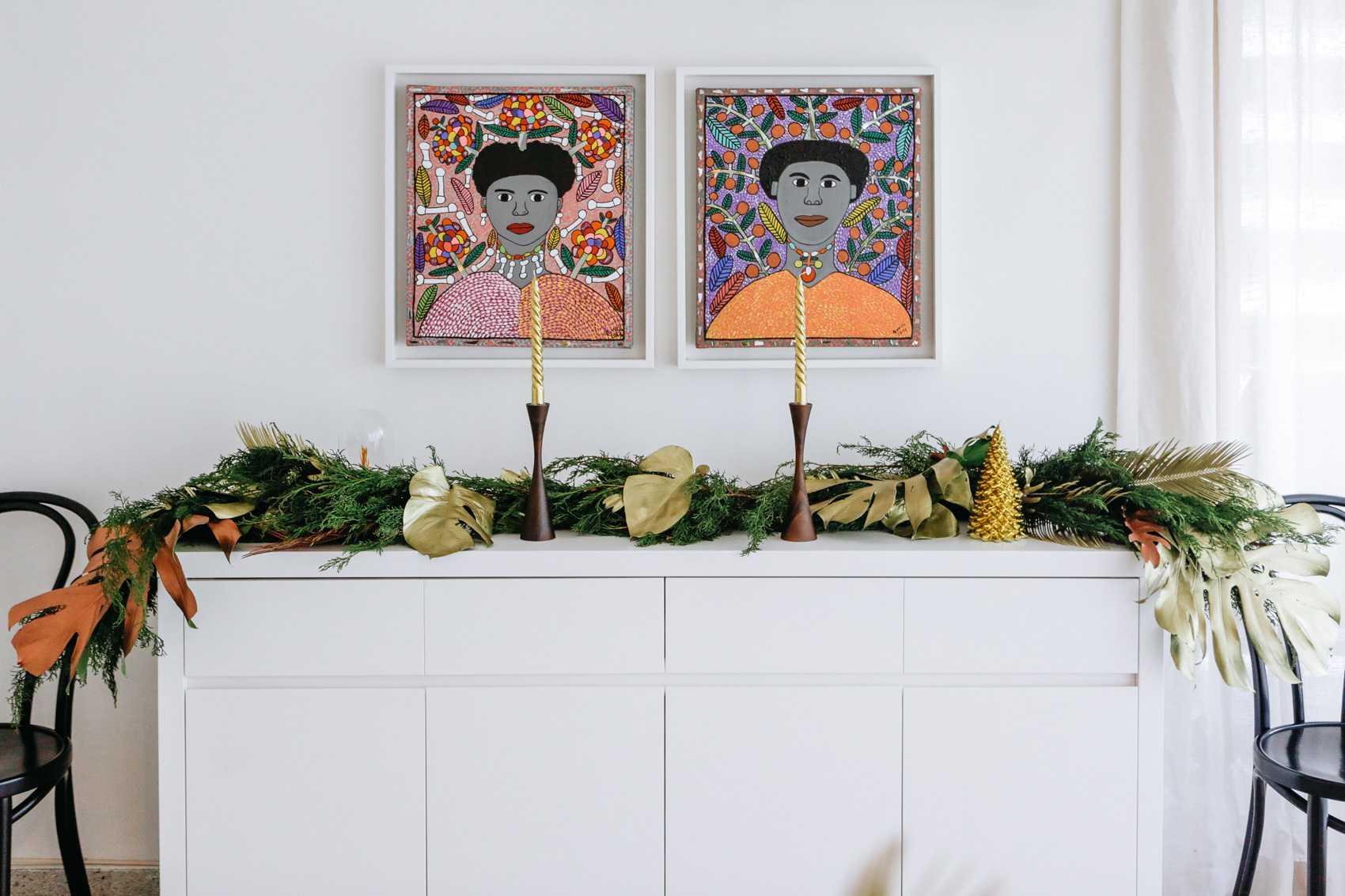 Thonet Chairs, white minimal sideboard with pine and monstera leaf Christmas garland, midcentury candle holders and afrocaribbean art