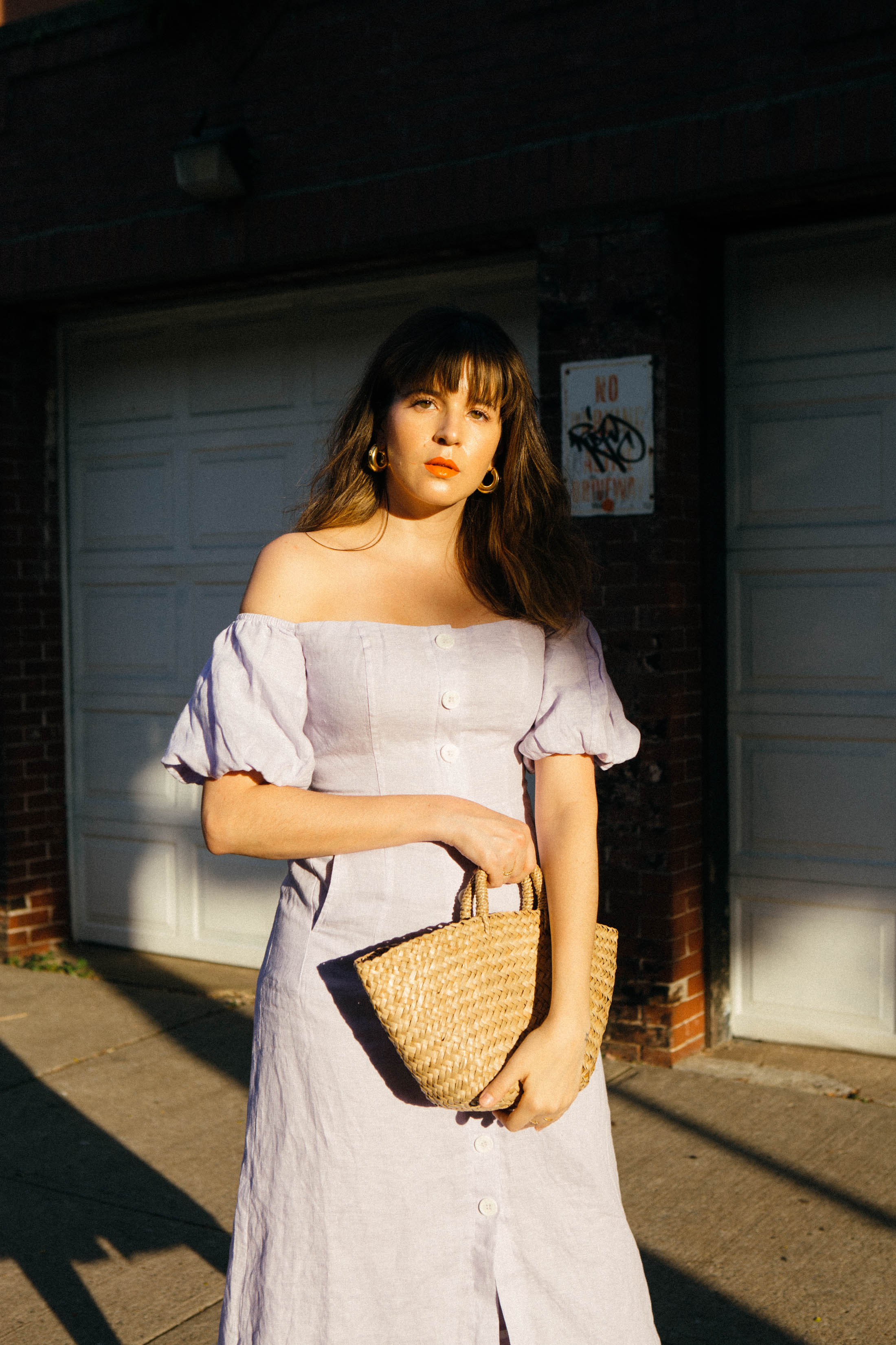 Maristella wears an off the shoulder dress and straw bag