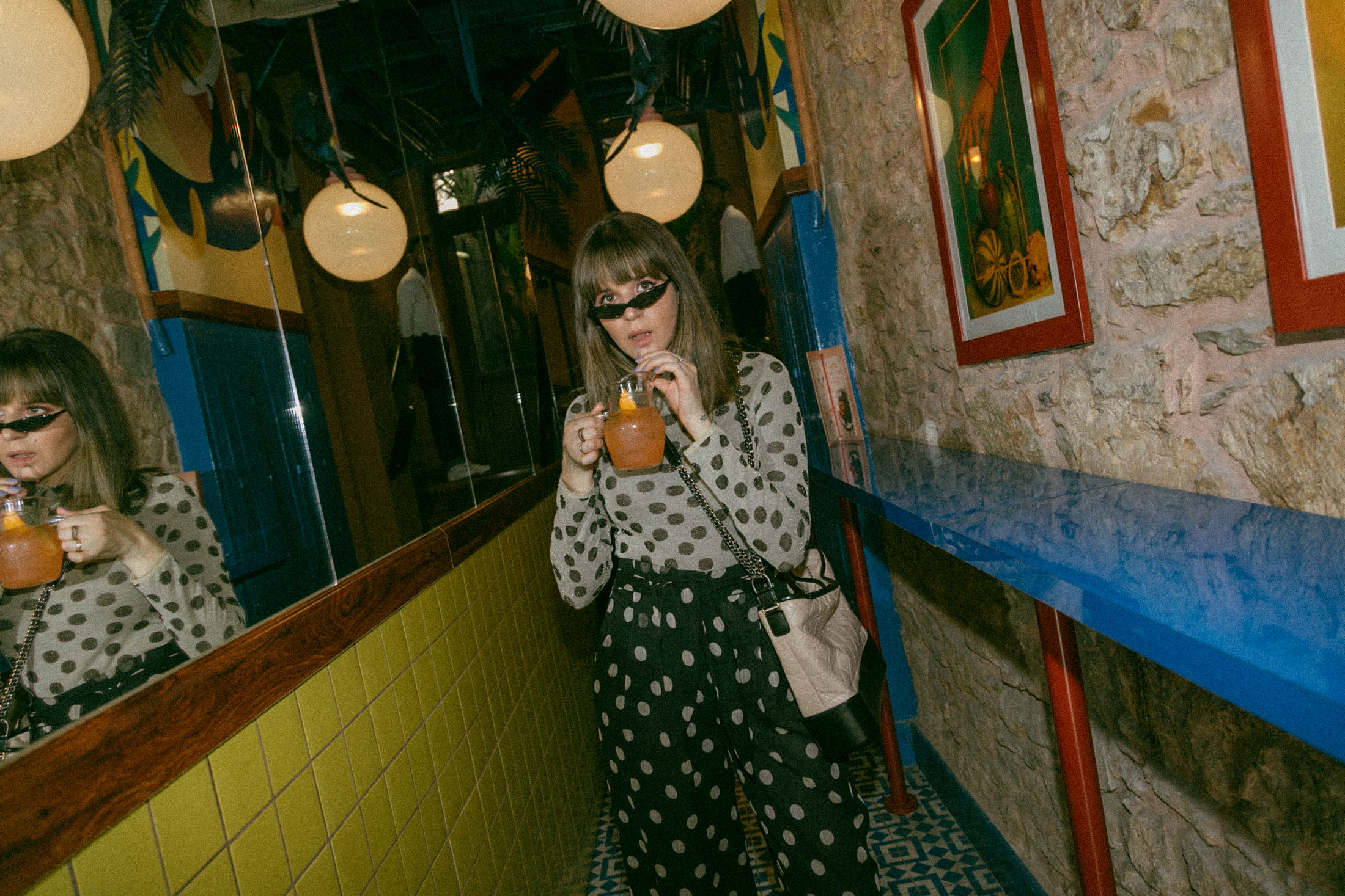 Maristella sipping on a cocktail at Fonda Paraiso in Panama, wearing a Nanushka top and pants polka dot set, Chanel Gabrielle bag and Giant Vintage Carolina sunglasses