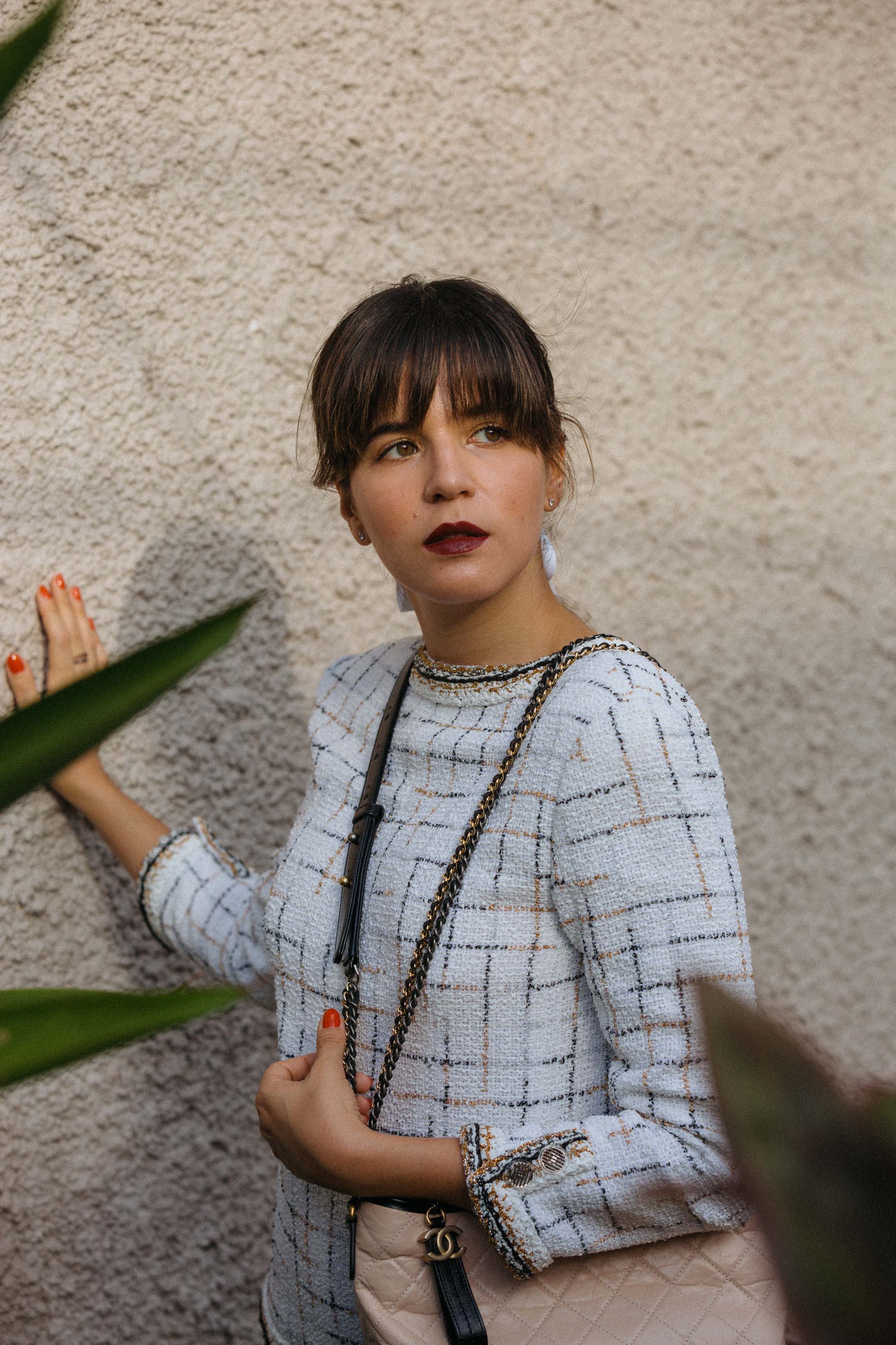 Maristella wears a backwards Chanel tweed jacket and the Chanel Gabrielle bag in the V style, bold dark purple lips and ponytail with bangs hairstyle