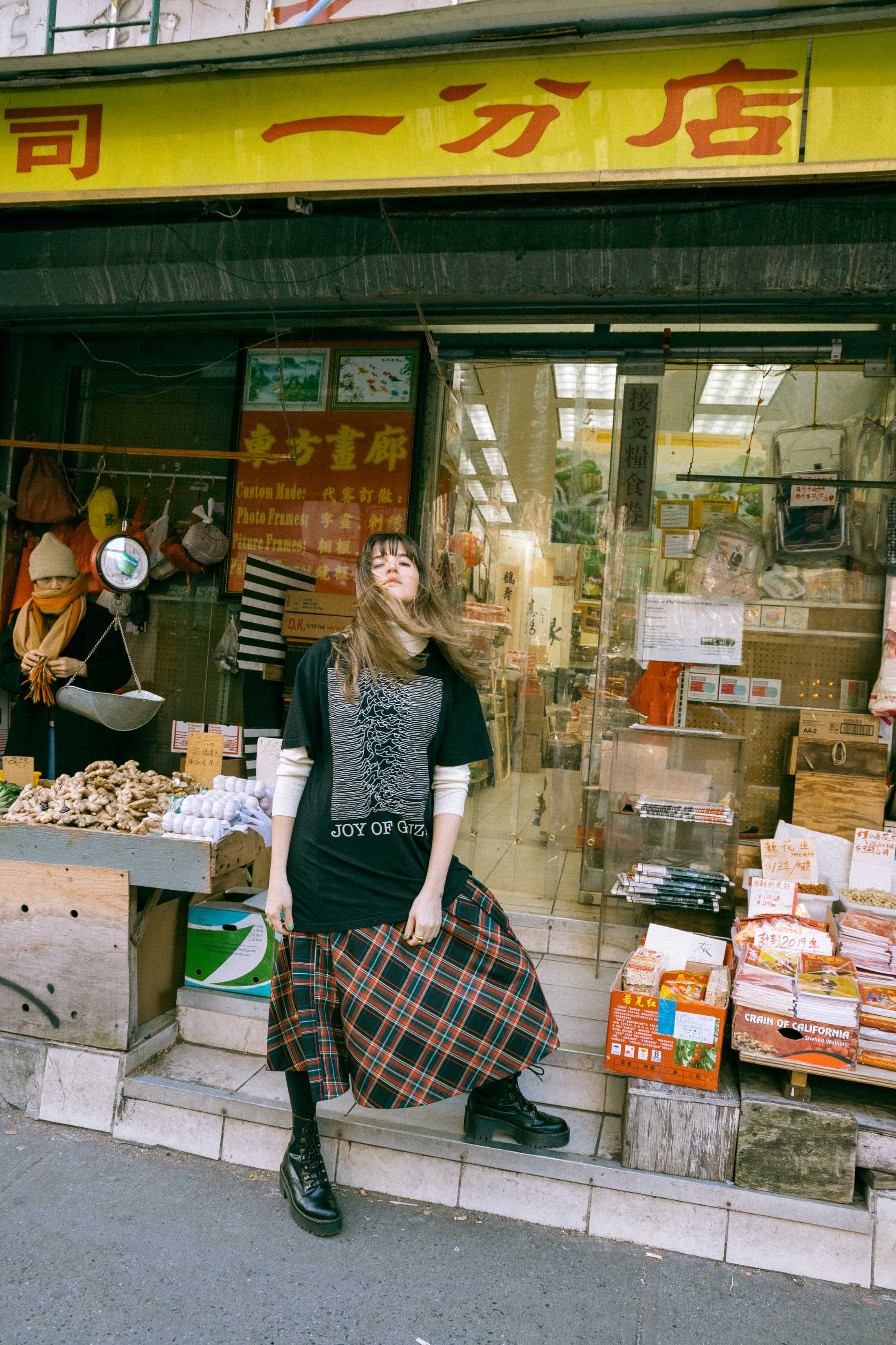 Maristella wears a turtleneck sweater under an oversize t-shirt, tartan skirt from Zara, Dr. Martens boots.