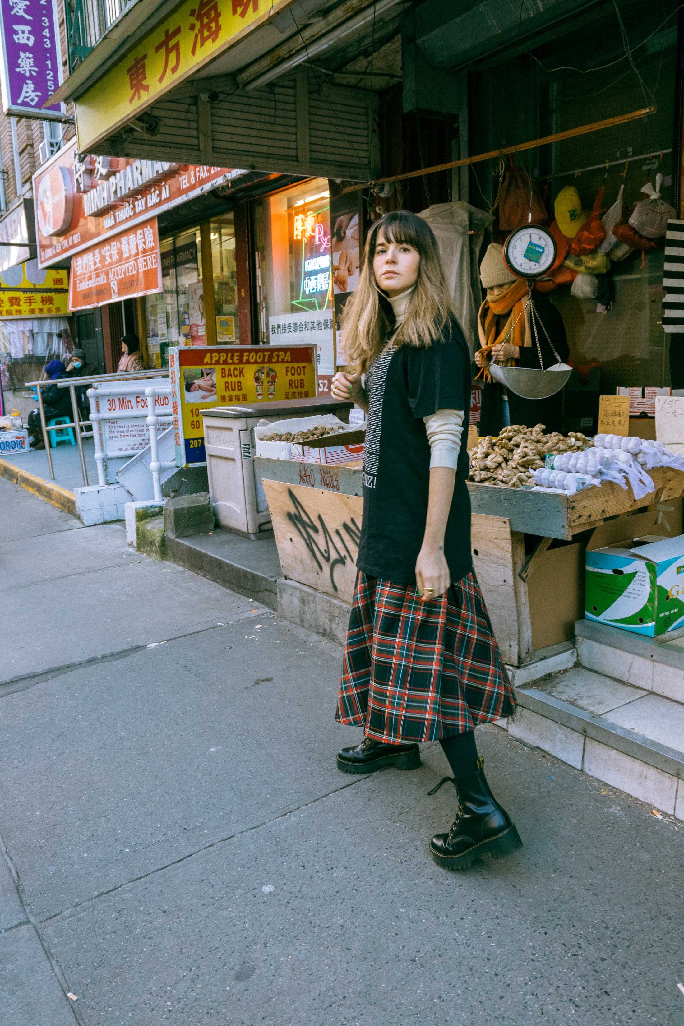 Maristella wears a turtleneck sweater under an oversize t-shirt, tartan skirt from Zara, Dr. Martens boots.