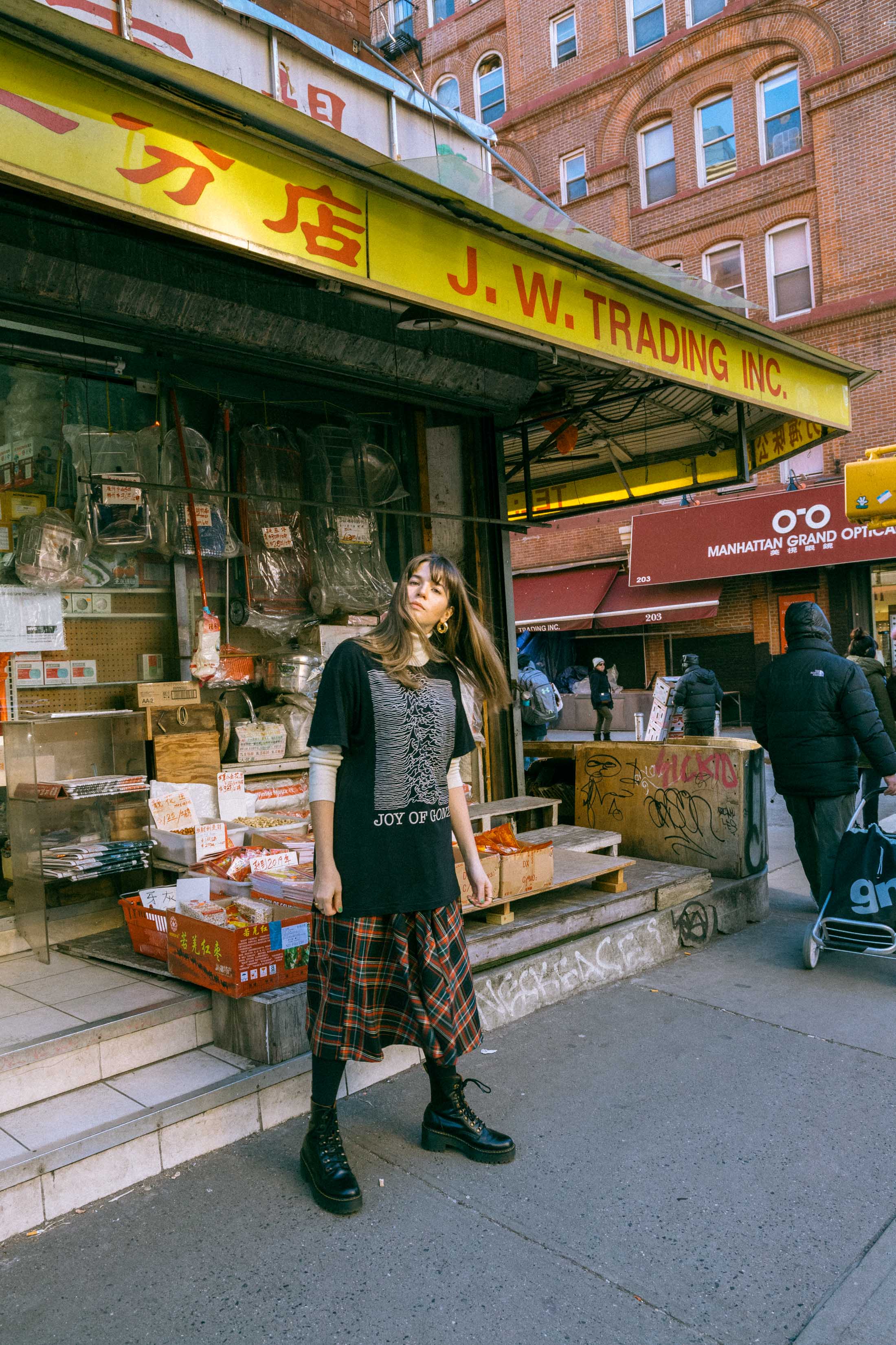 Maristella wears a turtleneck sweater under an oversize t-shirt, tartan skirt from Zara, Dr. Martens boots.