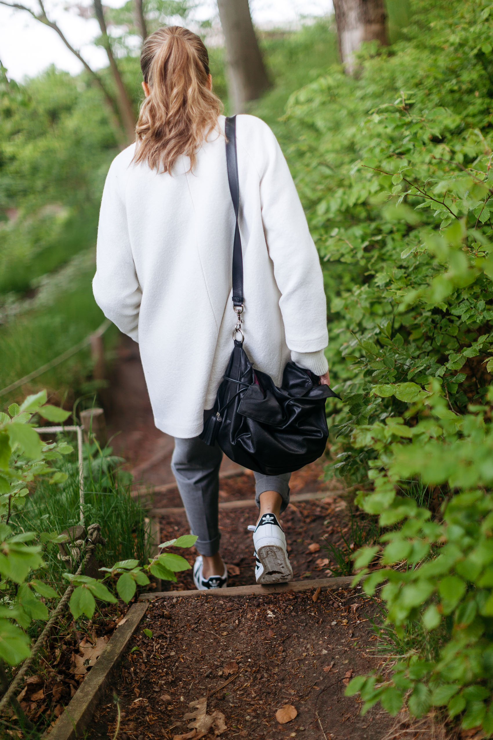 Maristella wearing a white coat, grey trousers, adidas Superstar sneakers and Loewe Flamenco Bucket bag