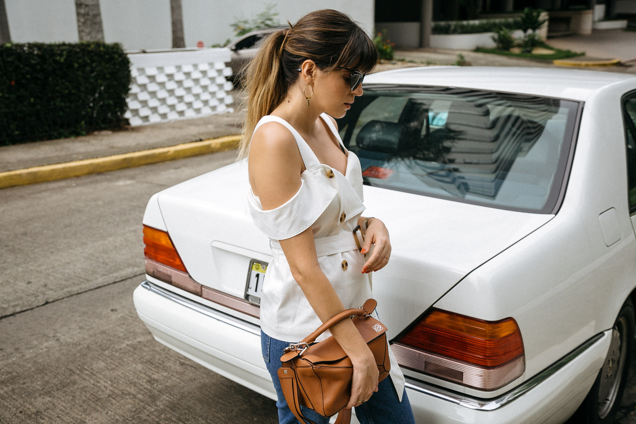 Maristella wears a white off the shoulder top from C/meo collective, Loewe tan leather Puzzle bag and jeans